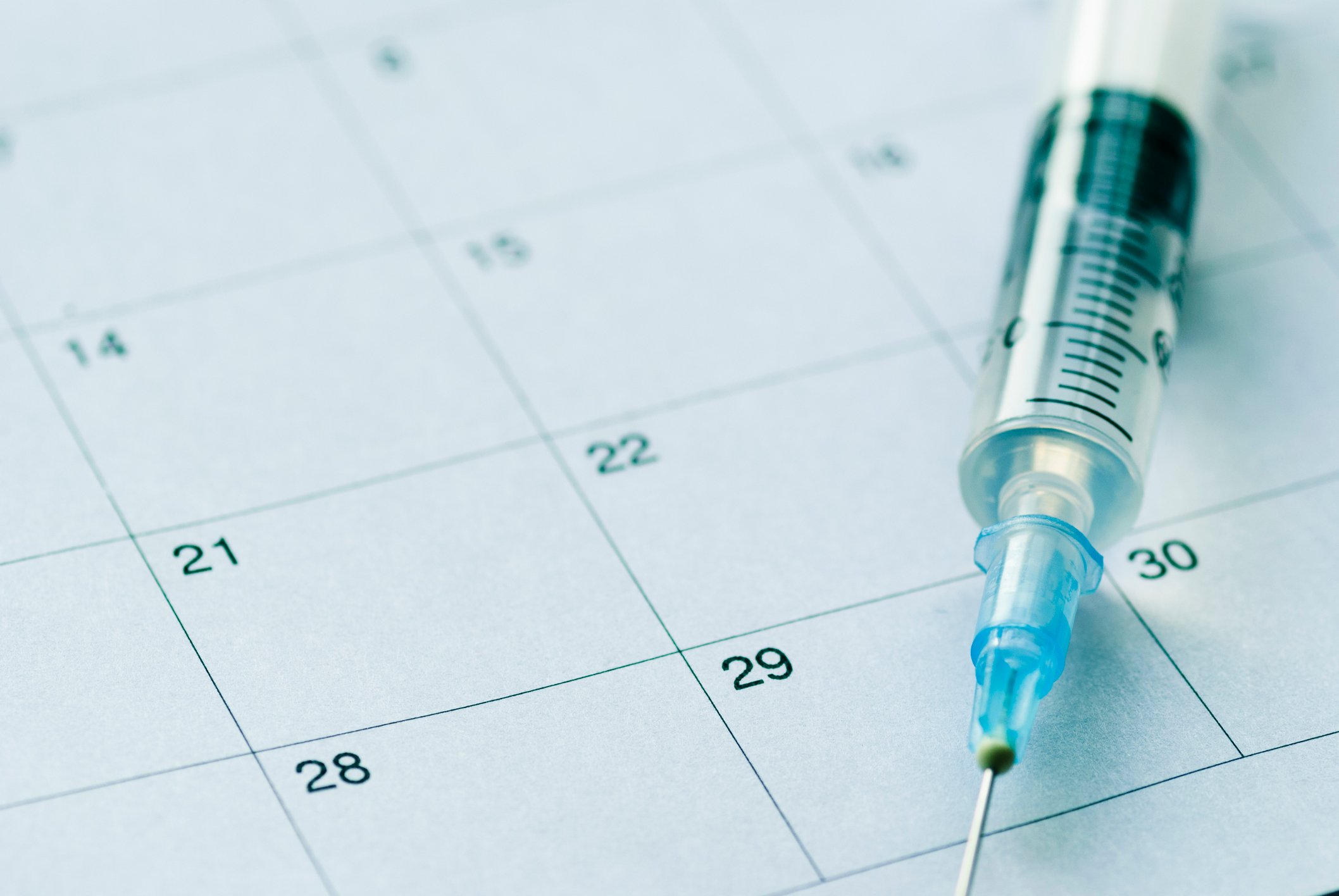 Syringe with needle on top of a calendar. 