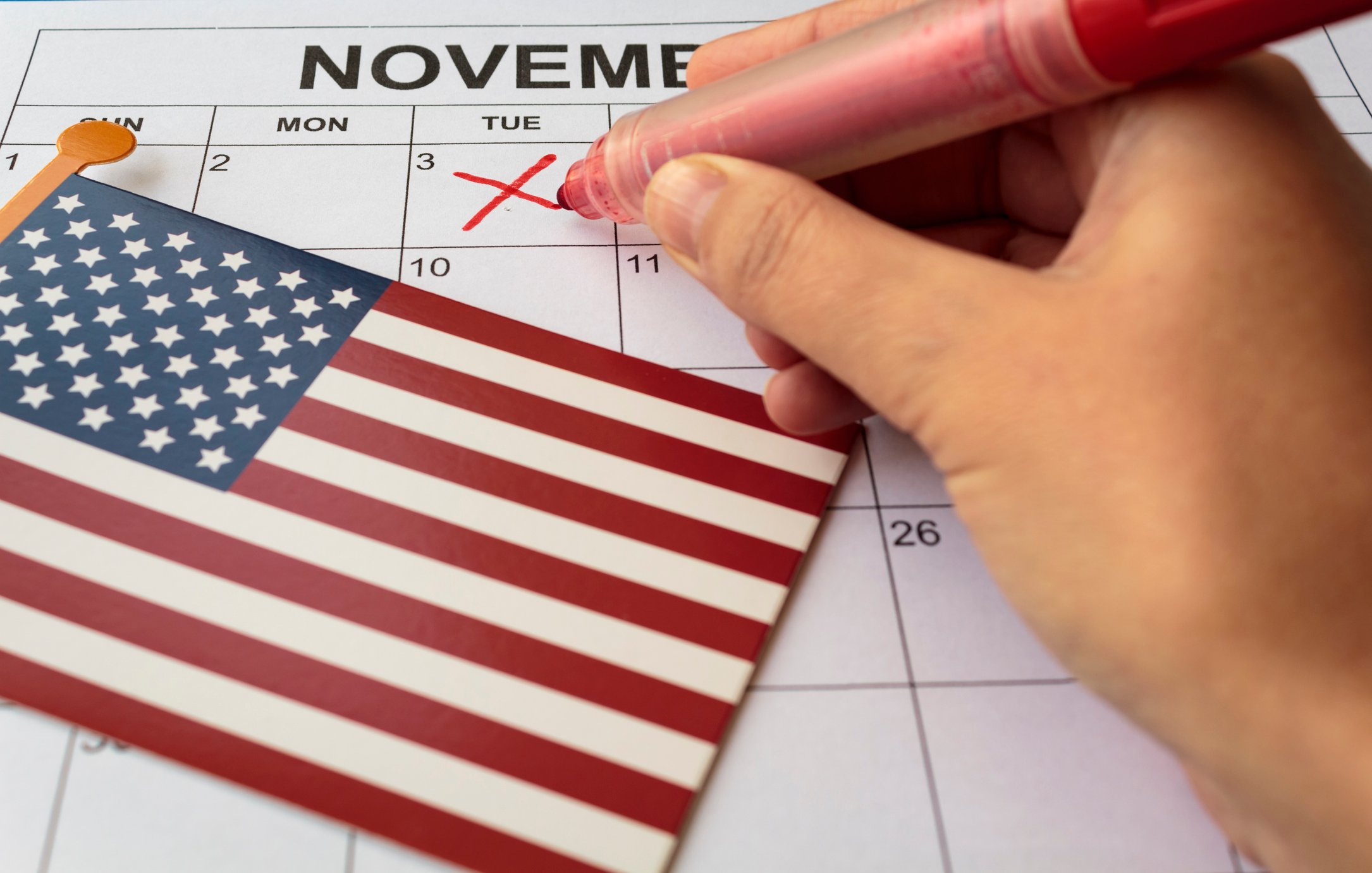 Hand holding a red marker making an X on Nov. 3 on a calendar with a small U.S. flag lying on top of the calendar