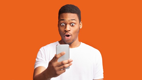 A young person looks at a cellphone with a shocked expression. 