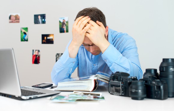 Man burying hand in his hand beside photos and digital cameras. 