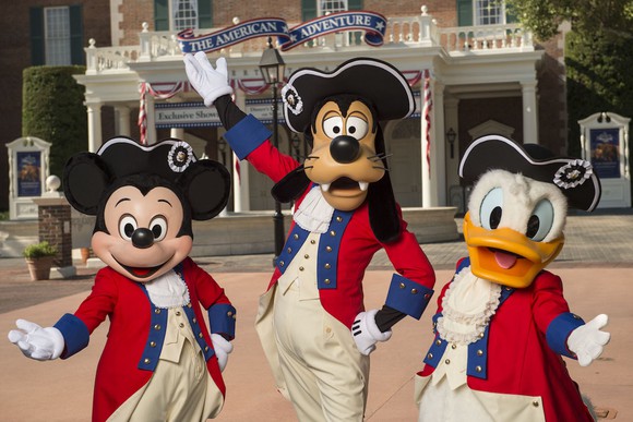 Mickey Mouse, Goofy, and Donald Duck posing in front of EPCOT's American Adventure pavilion. 