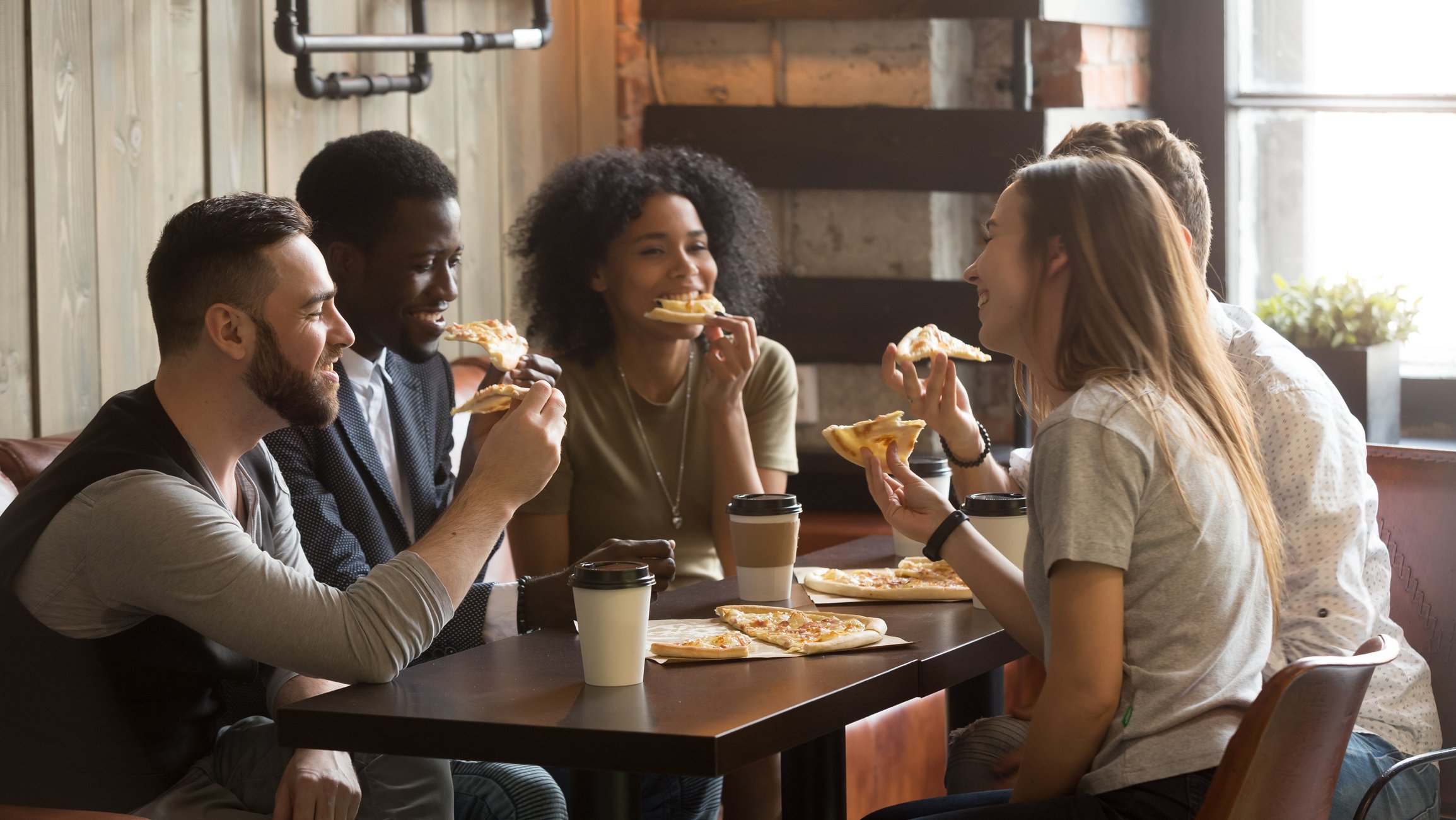 A group of friends eat pizza and drink coffee.
