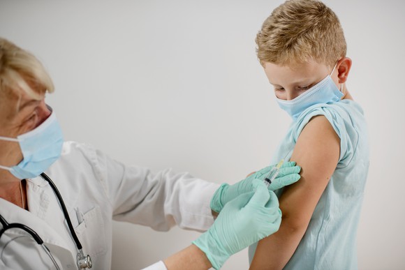 A doctor administers a vaccine to a child; both are wearing face masks.