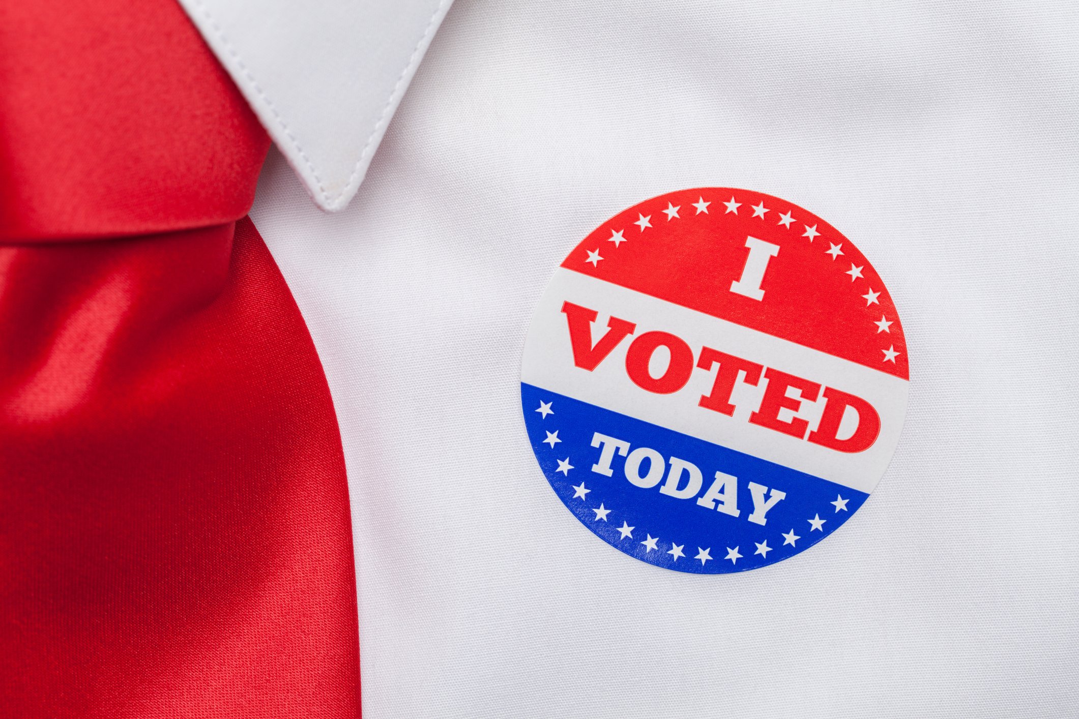 A person with a white shirt and red tie with a sticker that says I voted today on the lapel