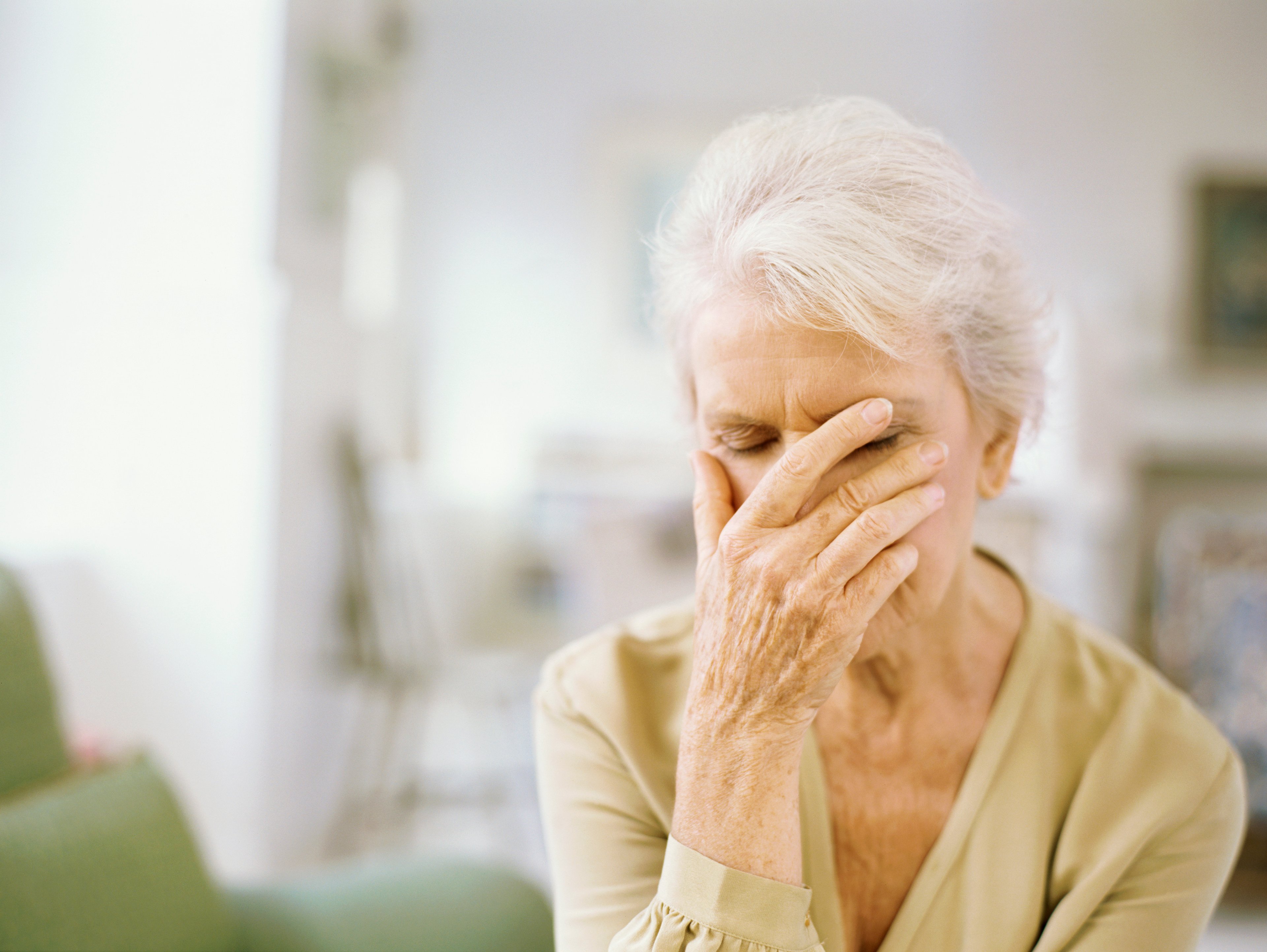 A senior woman buries her face in her palm out of frustration.