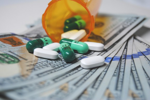 A bottle of pills spills onto a bed of hundred dollar bills.