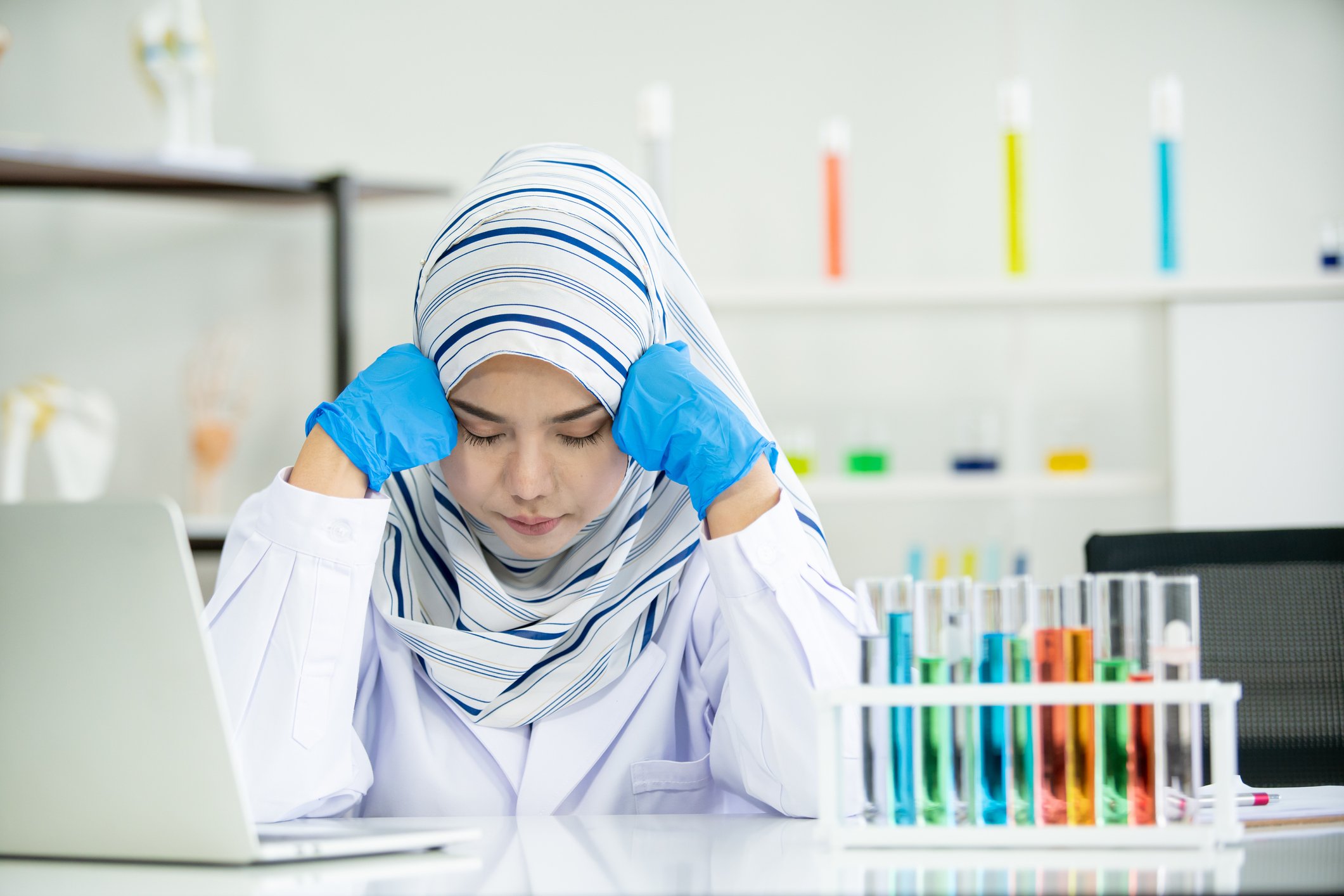Scientist in lab with test tubes and laptop, looking exasperated