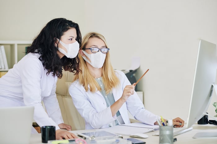 Two healthcare professionals wearing face masks, looking at a PC monitor