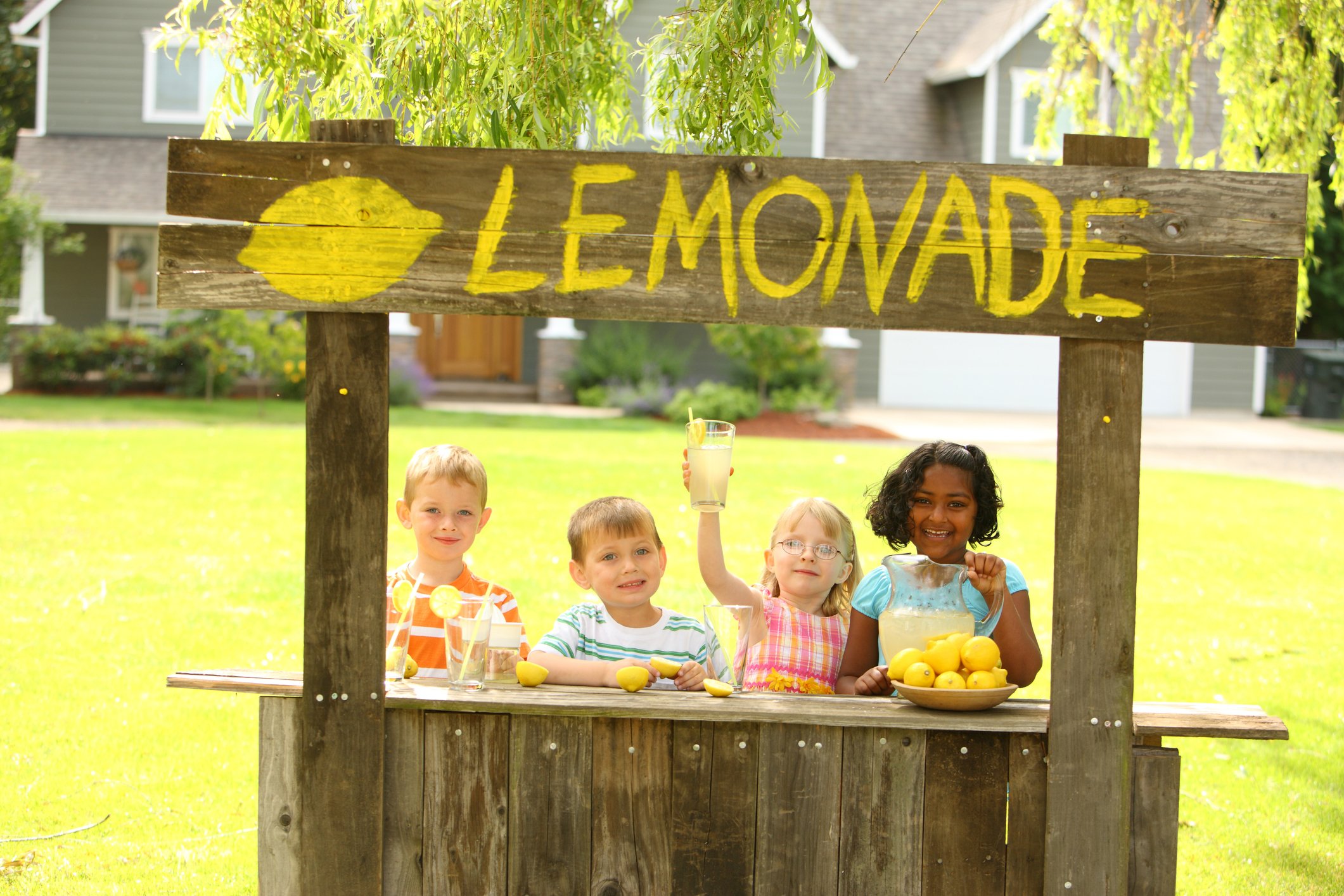 Four kids at a lemonade stand in the front yard.