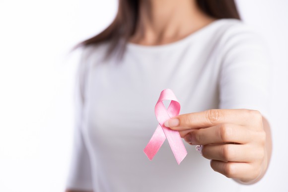 A lady holding a pink ribbon forward signifying breast cancer awareness.