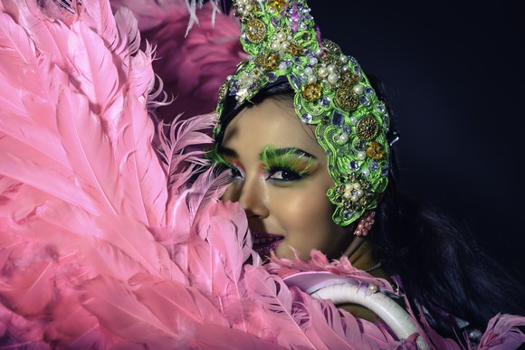 A Las Vegas cabaret showgirl looking out from behind pink feathered "wings," wearing a green and white headdress.