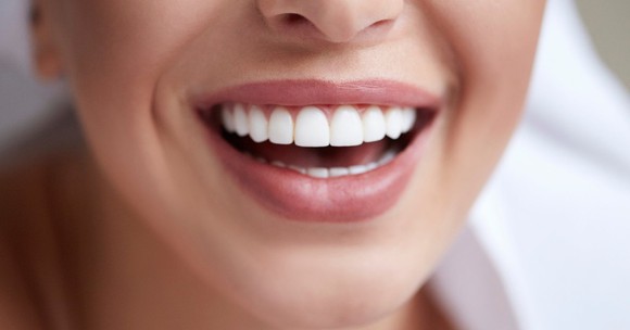 Lower half of woman's face with a bright smile and perfectly aligned front teeth.
