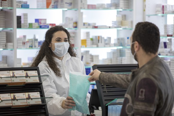 Pharmacist wearing mask and handing customer a prescription