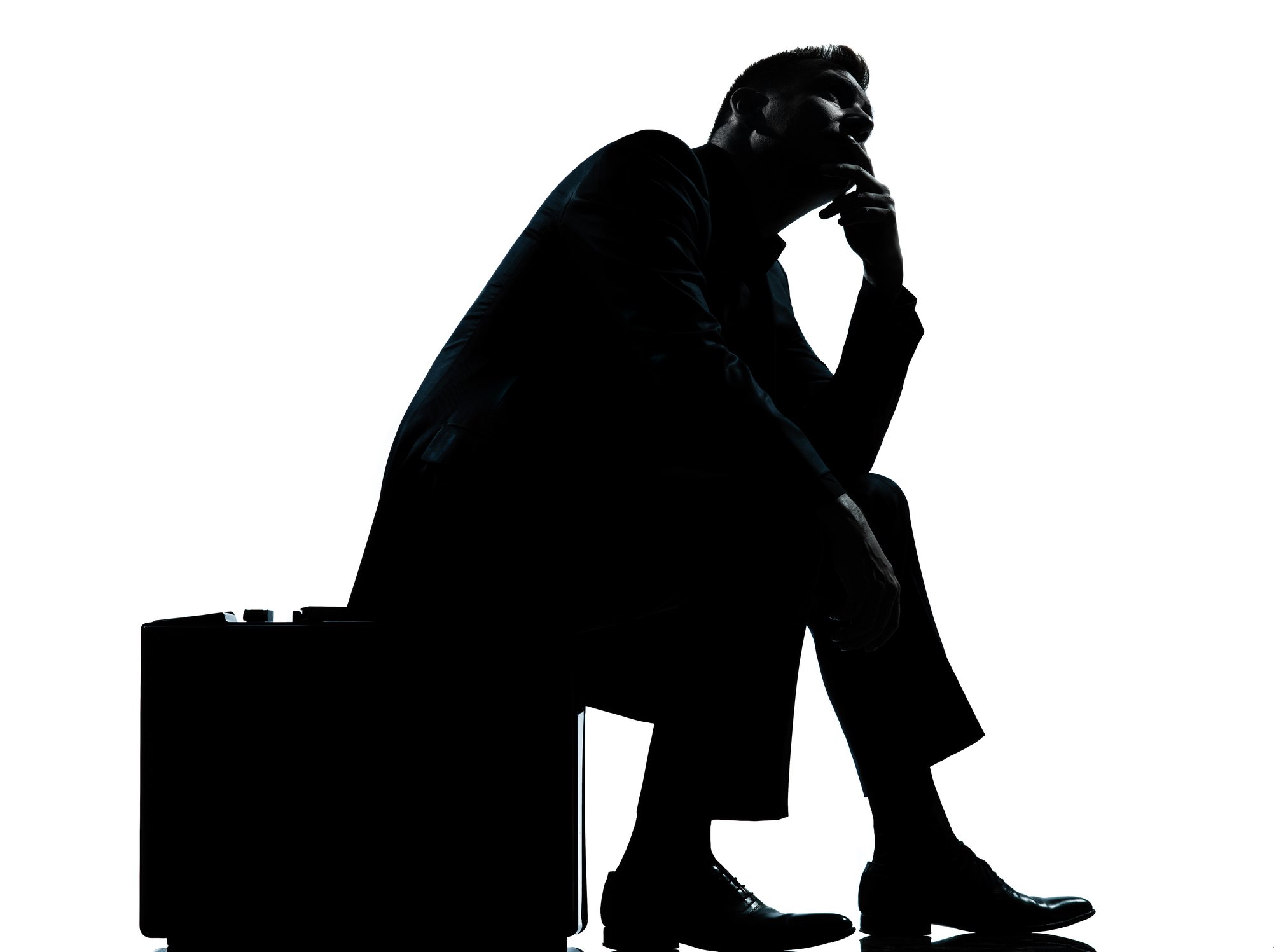 Silhouette of a businessman sitting on his briefcase, apparently in deep thought.