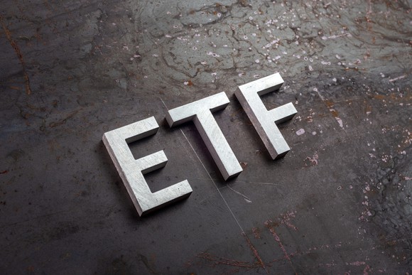Big block letters lying on a brown surface that read ETF. 