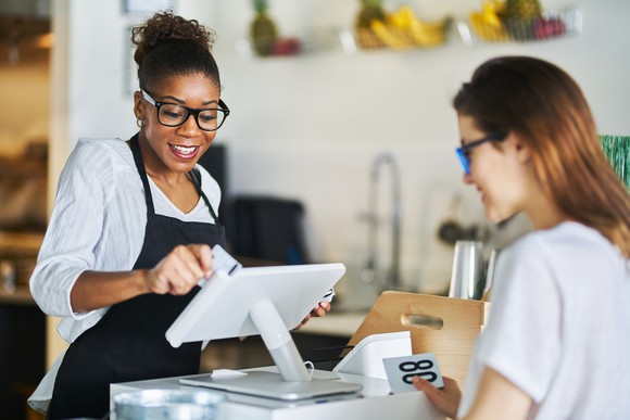 Female cashier swipes customer's card through a point of sale system while customer stands in foreground.