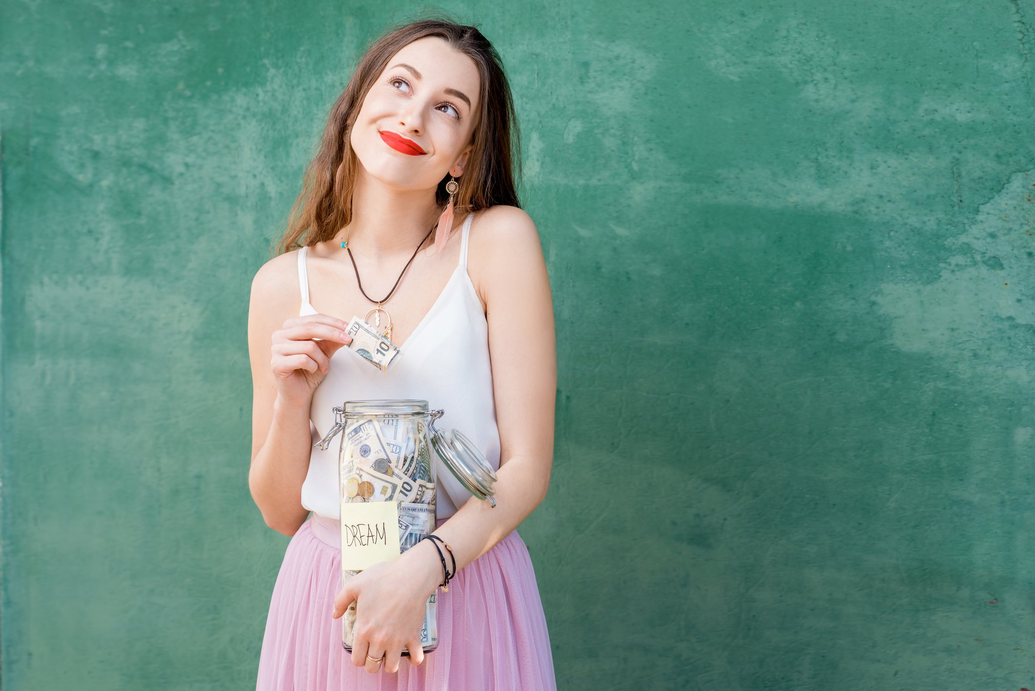 Smiling young woman holding jar of cash.