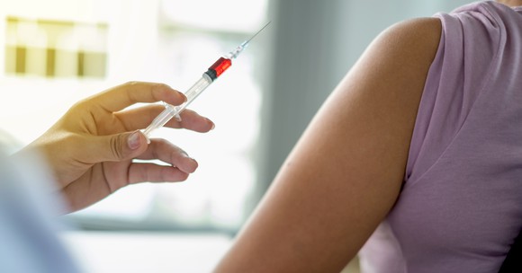 Physician's hand holding a syringe next to a patient's arm. 