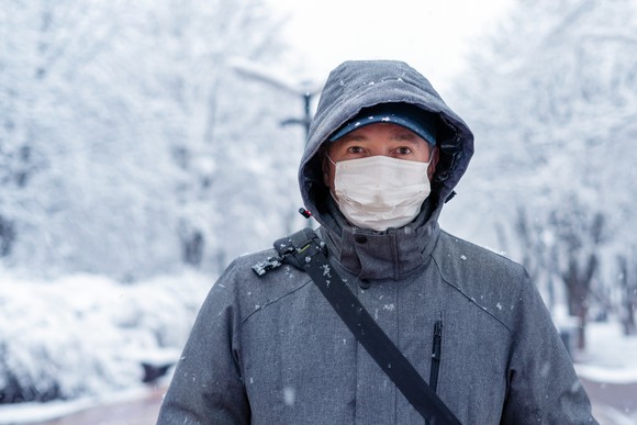 A man wearing a medical mask in a snowy background.