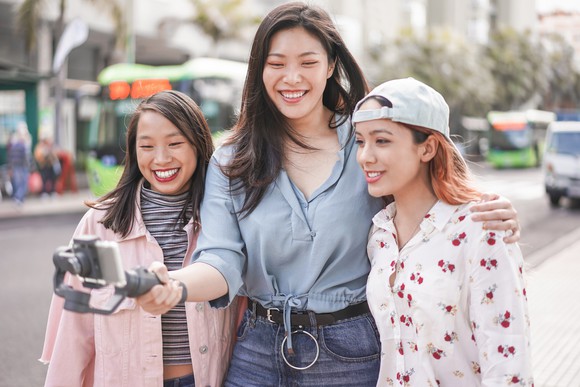 Three young women stream a live video on a smartphone.