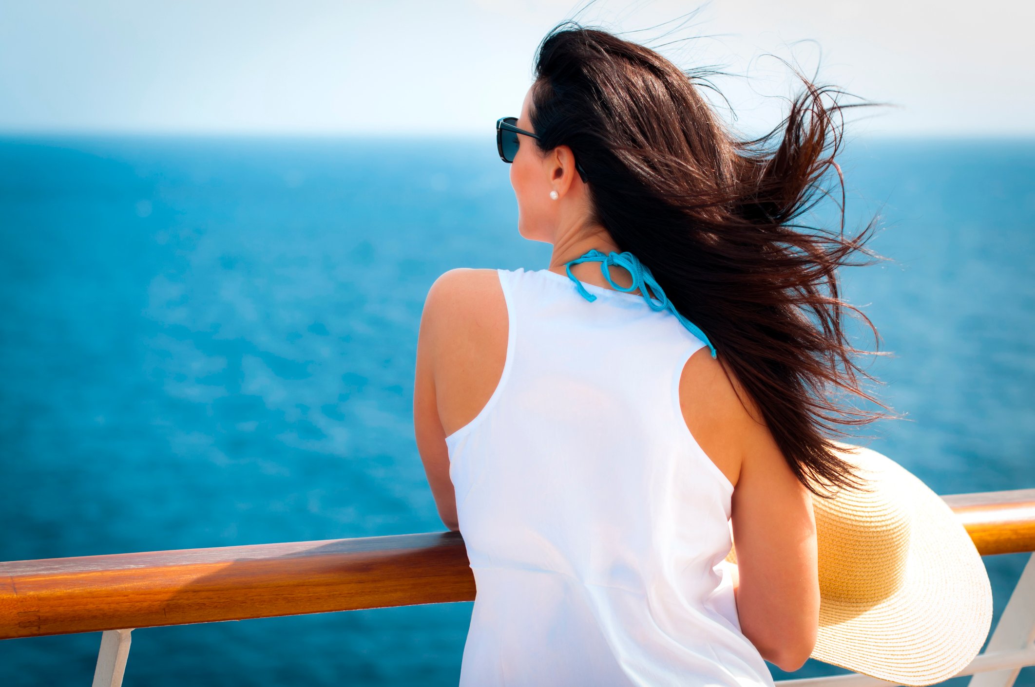 A woman stands on a cruise ship deck and looks out to sea.