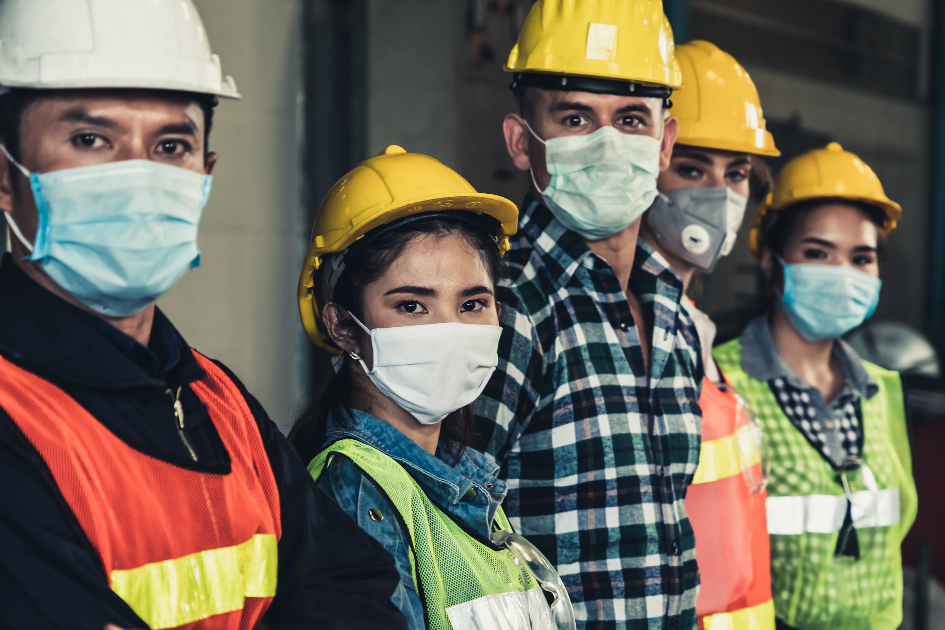 A line of 5 young men and women wearing hard hats, safety vests, and masks.