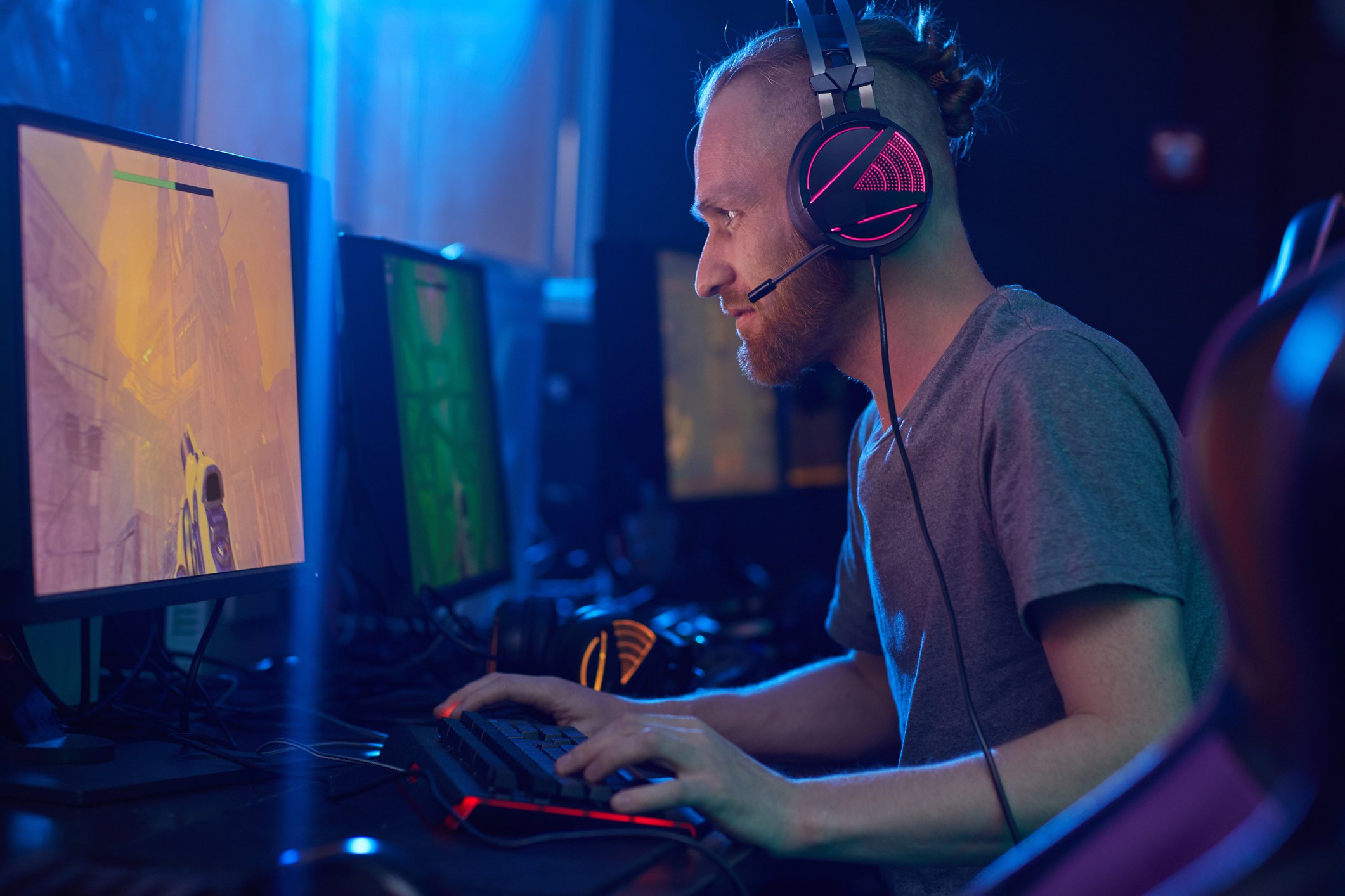 An man sitting at a computer playing a video game while wearing a headset. 