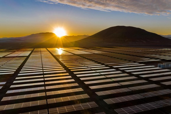 Sun rising over mountains, with solar panels in foreground.