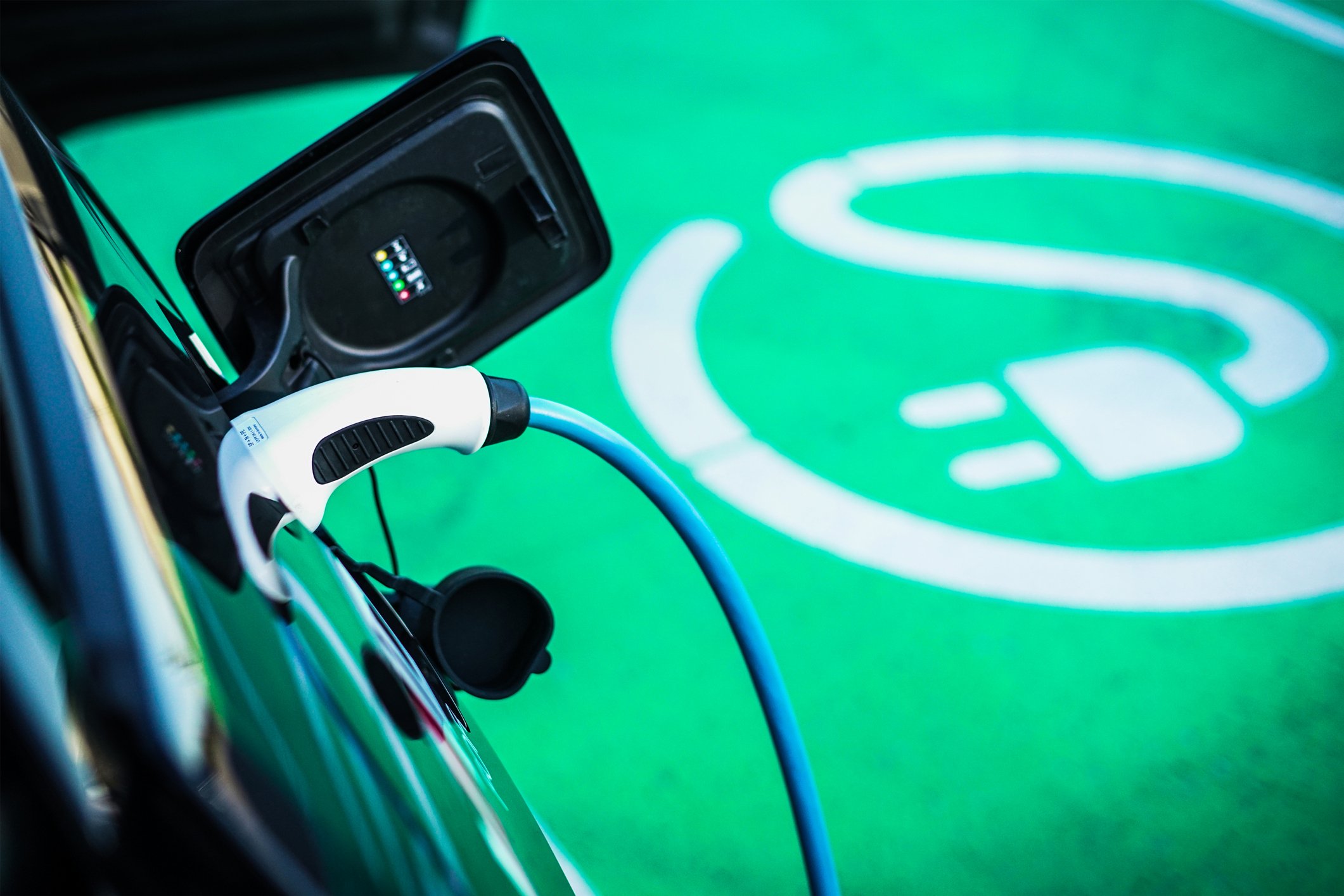 Angled view of an electric vehicle connected to a power source at a charging station.