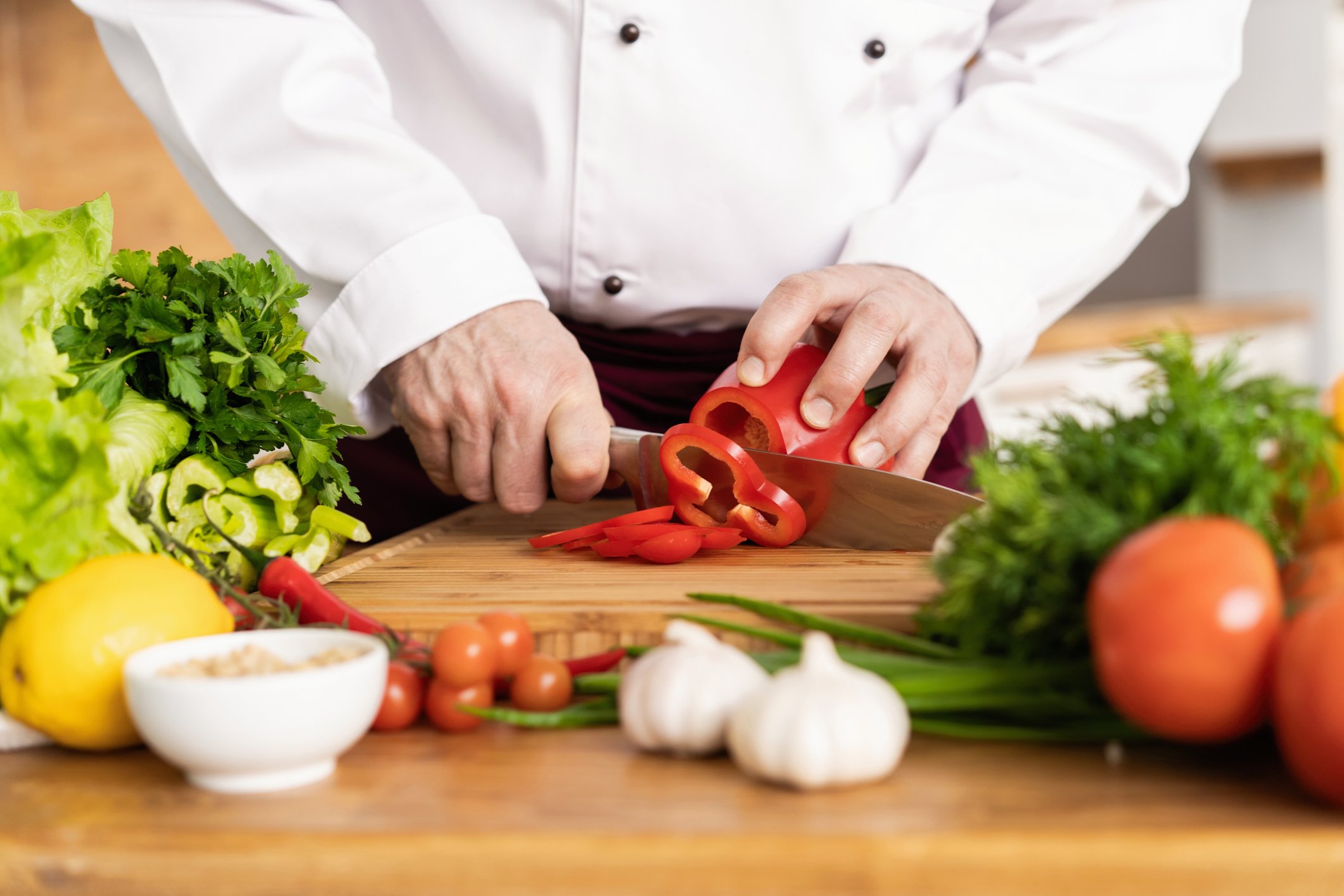 Chef cutting a pepper with additional vegetables on the cutting board.