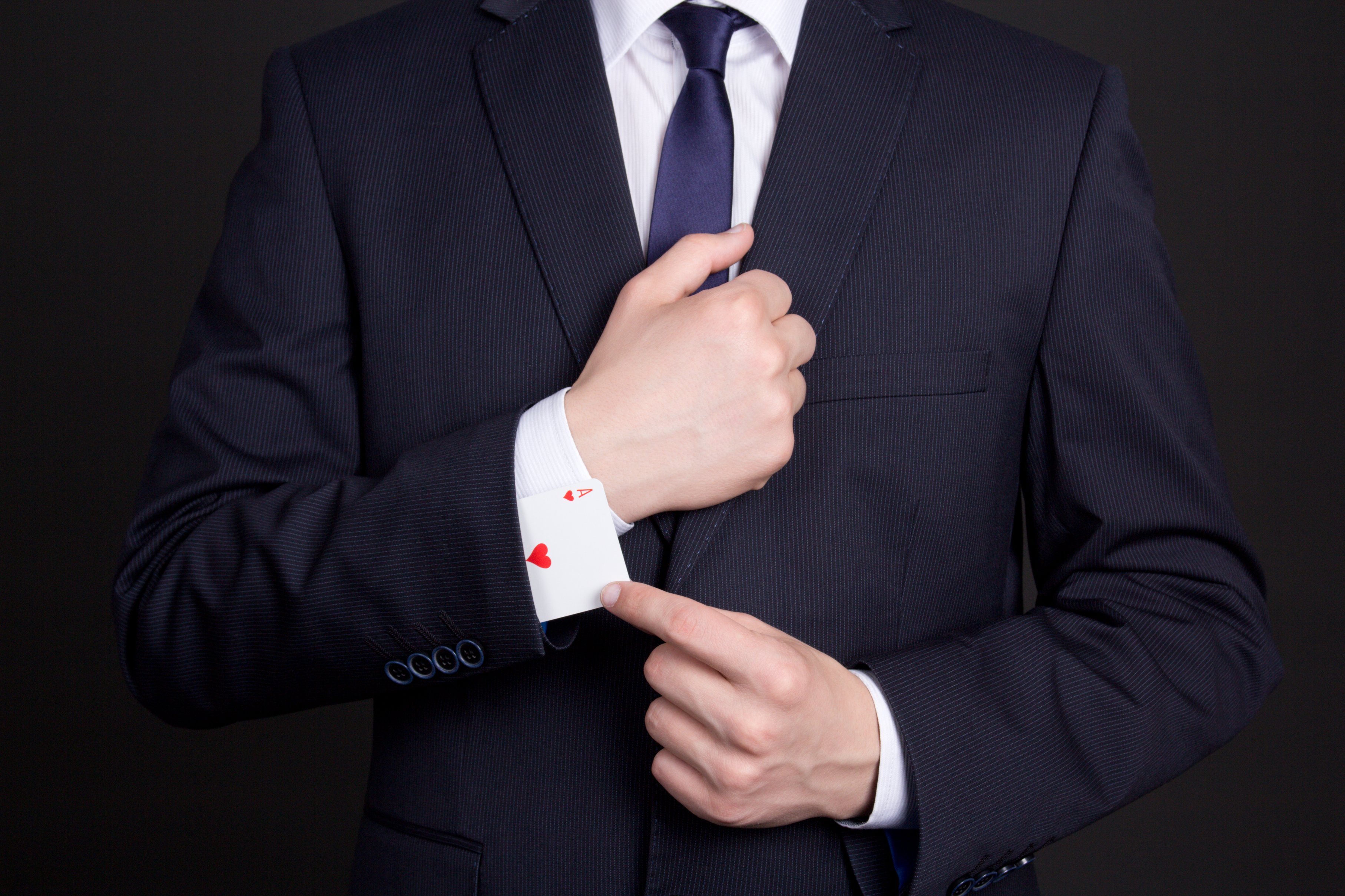 A man in a suit reveals an ace playing card hidden in his sleeve.
