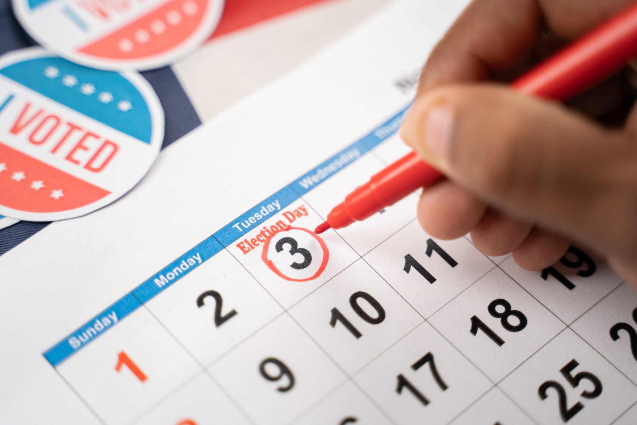 Person circles election day, November 3rd, on a white calendar, with "I Voted" stickers sitting beside.