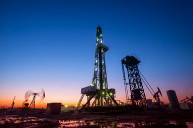 A drilling rig near a pump at dusk.