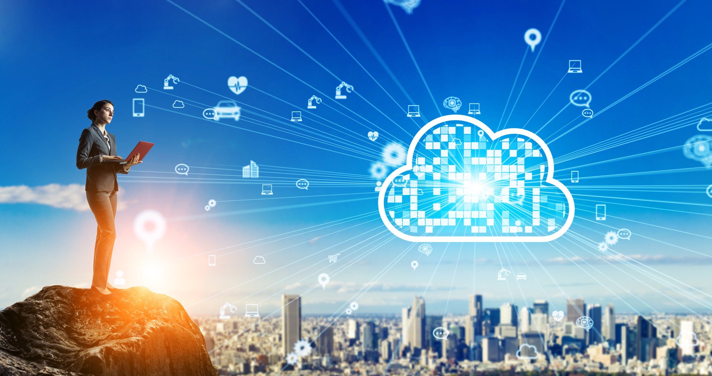 Woman standing on a mountain top above a city as she holds her laptop and connects to the cloud hovering above the city.
