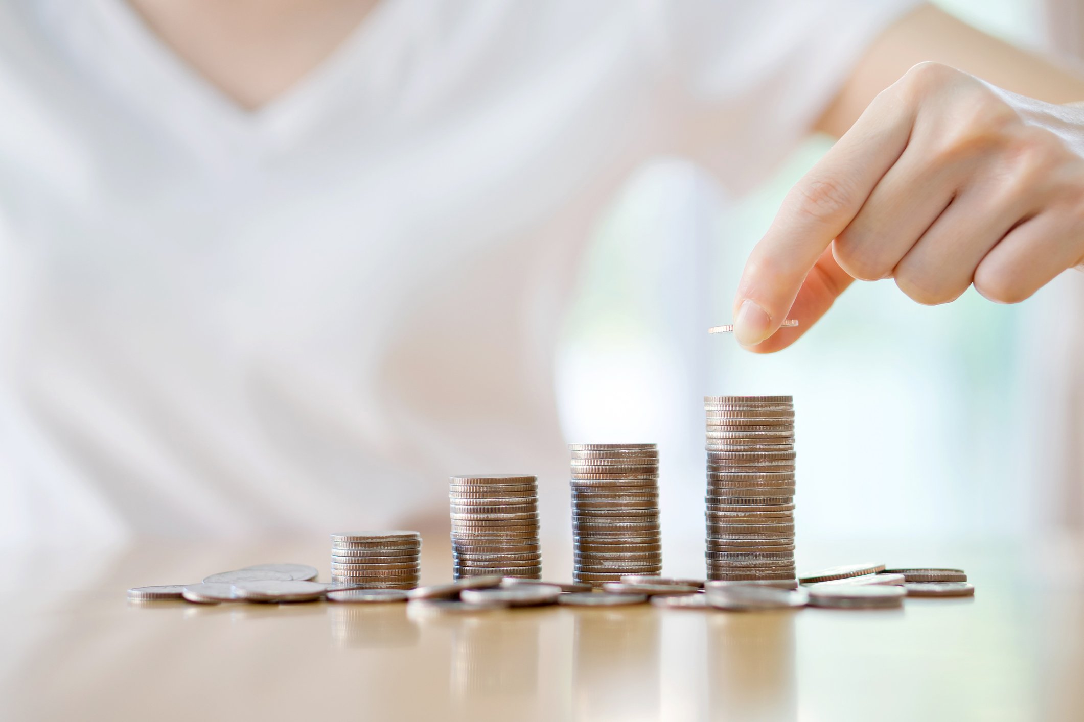 A casually dressed young person stacks coins in piles of rising height.