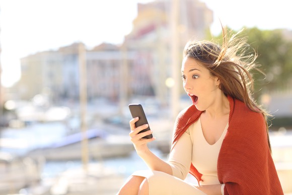 A young woman stares at her smartphone in amazement.