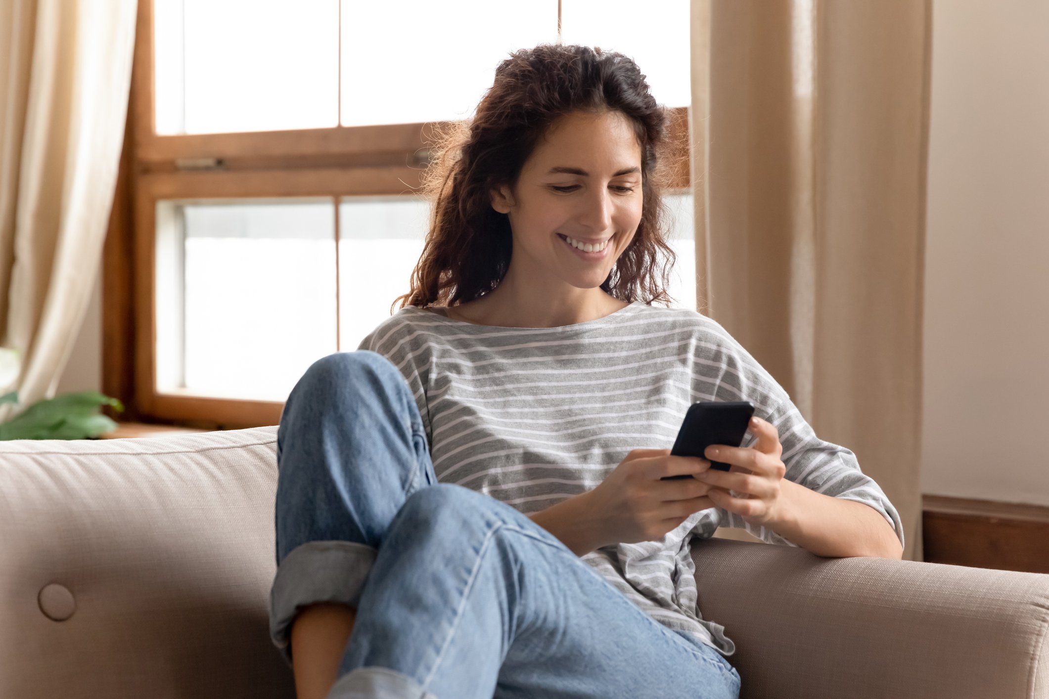 Woman sitting on a couch smiling as she stares at her smartphone