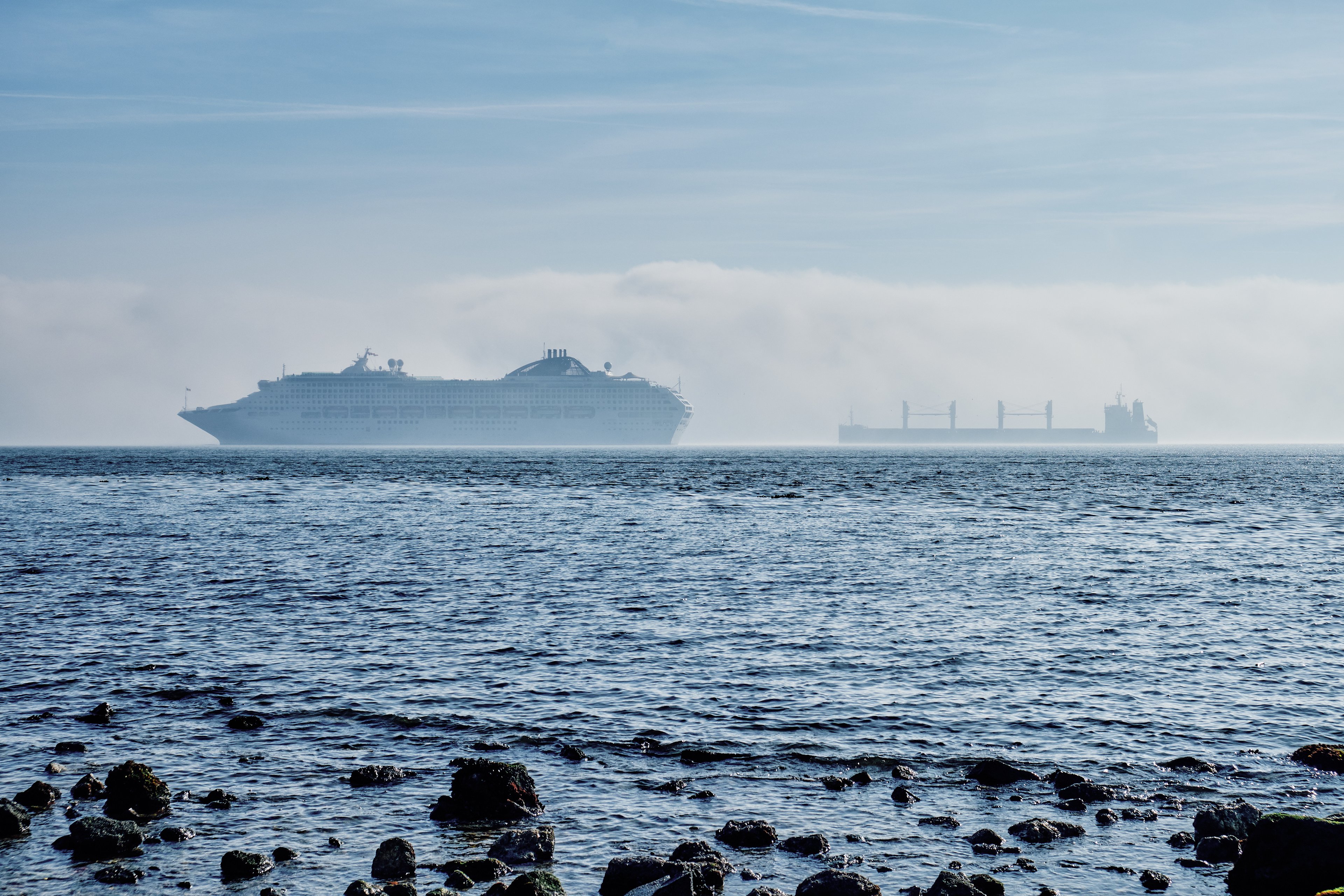 A cruise ship seen through a sea mist, passing a cargo vessel, off Lisbon, Spain.
