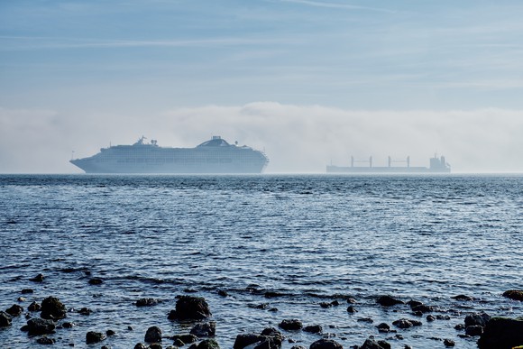 A cruise ship seen through a sea mist, passing a cargo vessel, off Lisbon, Spain.