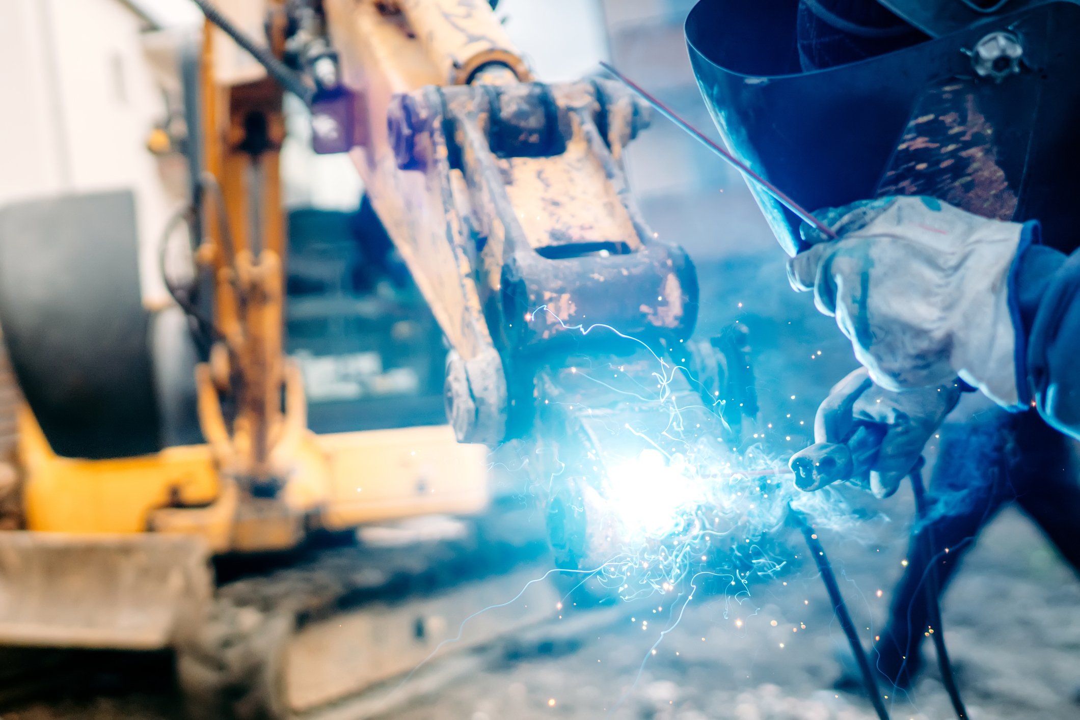 A welder works on industrial machinery at a construction site. 