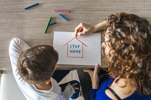 A woman and child illustrate a house enclosing the words "stay home".