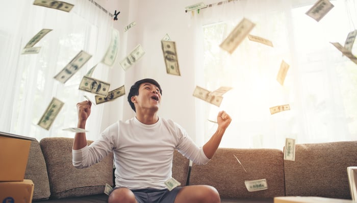 A man on a couch celebrates as money flies through the air around him.