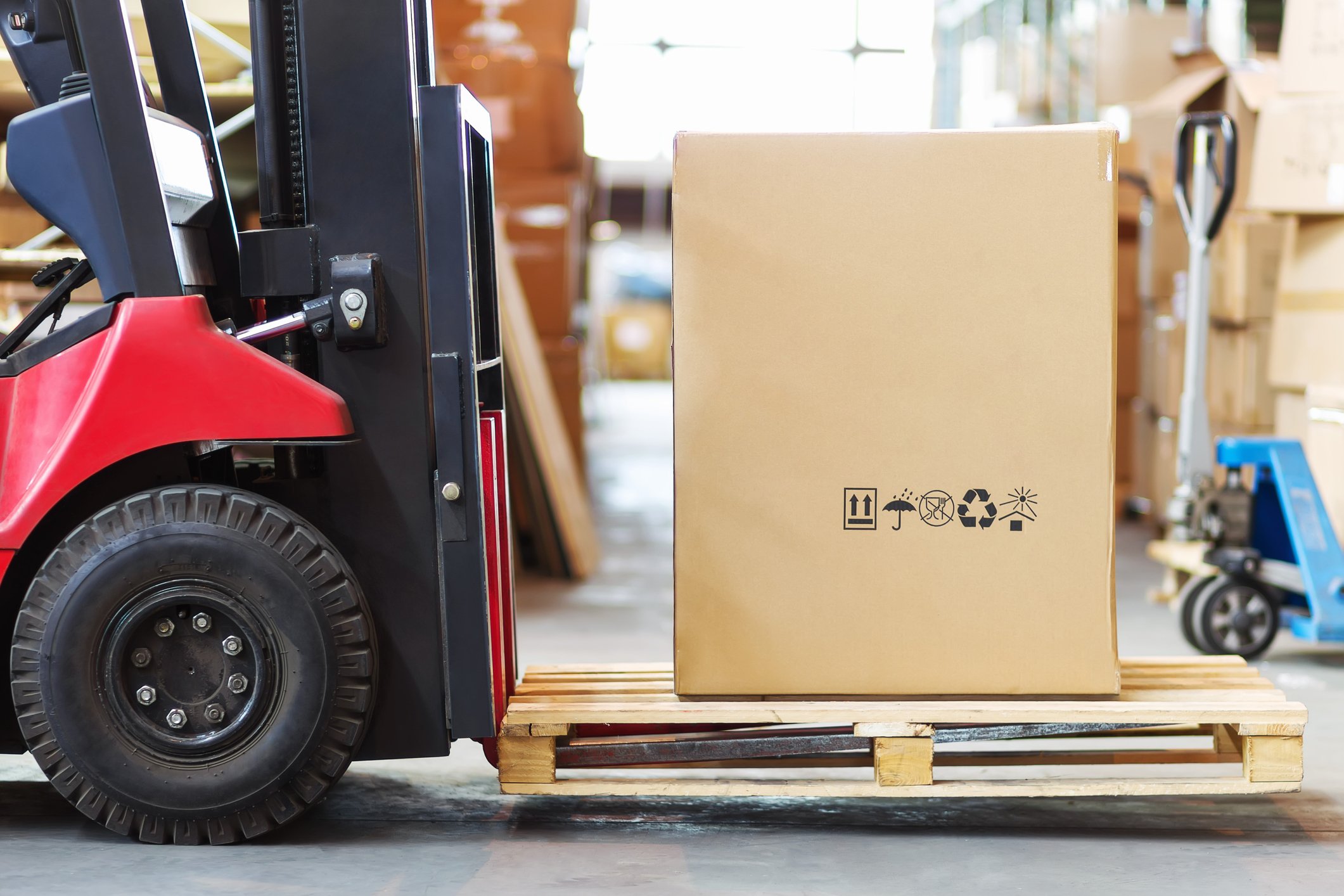 A red forklift moving a large box, possibly containing furniture, at a warehouse.