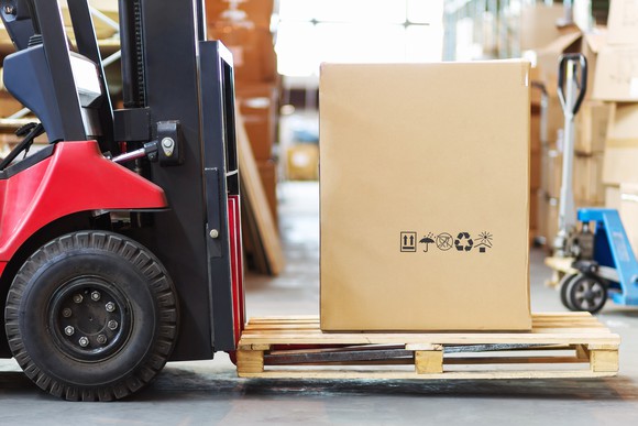 A red forklift moving a large box, possibly containing furniture, at a warehouse.