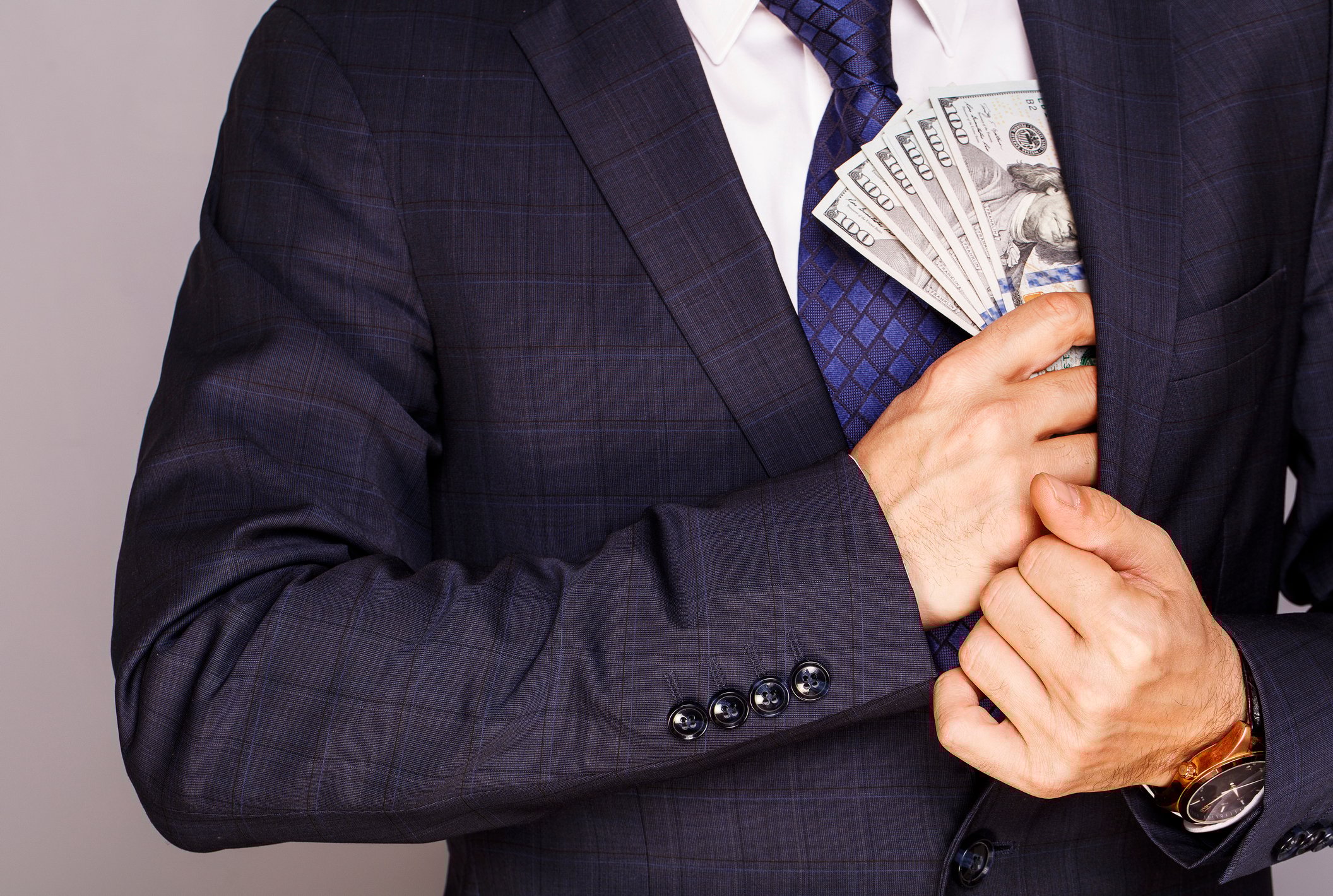 An investor tucks a handful of $100 bills into an inside pocket of his suit. 