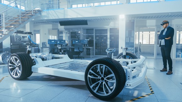 Automotive frame with tires and one person standing nearby.