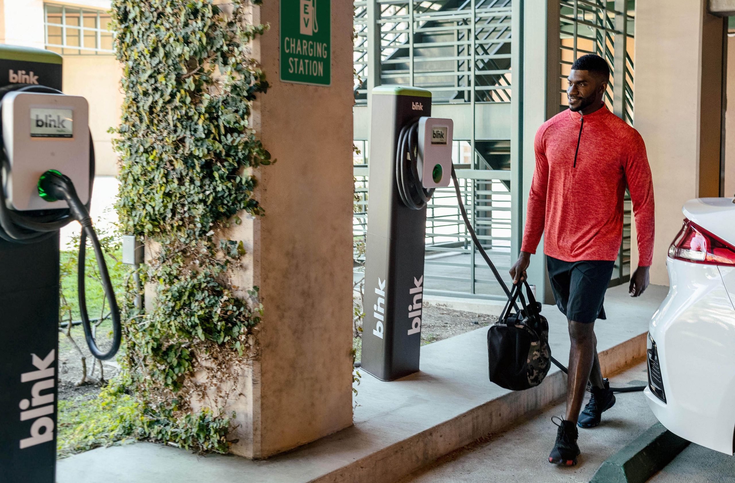 Man walking up to a Blink charger with a car next to him already charging