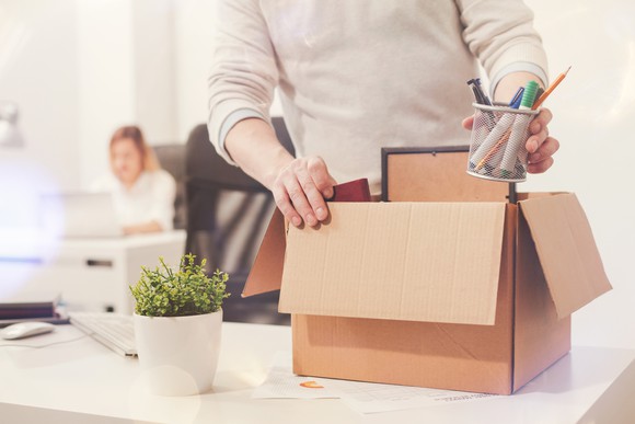 A laid off worker packing their desk items into a cardboard box.