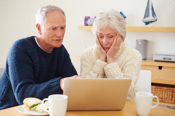 Older woman putting hands on face next to older man at laptop