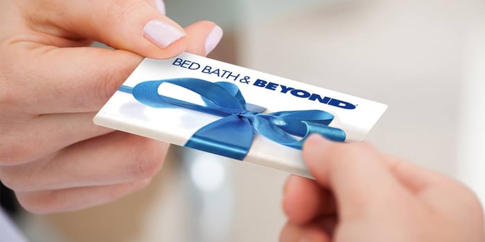 Two people's hands holding a Bed Bath & Beyond gift card